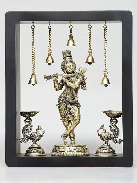 Brass Lord Krishna wall hanging with hanging bells and oil-lamp bowls in a framed display