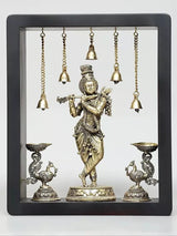 Brass Lord Krishna wall hanging with hanging bells and oil-lamp bowls in a framed display