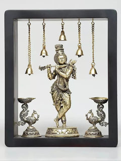 Brass Lord Krishna wall hanging with hanging bells and oil-lamp bowls in a framed display