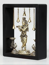 Brass Lord Krishna wall hanging in dark frame with hanging bells and lamp bowls at bottom