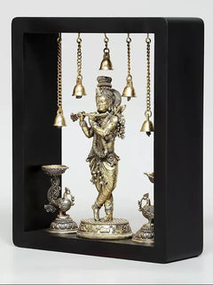 Brass Lord Krishna wall hanging in dark frame with hanging bells and lamp bowls at bottom