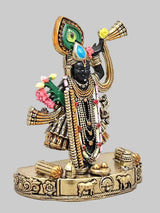 Small brass Krishna statue in gold attire with colorful flowers and beadwork, raised arms, base