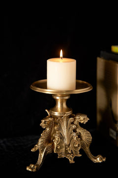 Brass candle stand with lion ornament base and round top, holding a lit pillar candle