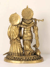 Brass Radha and Krishna statue, side view with peacock-like fan behind, cow at base
