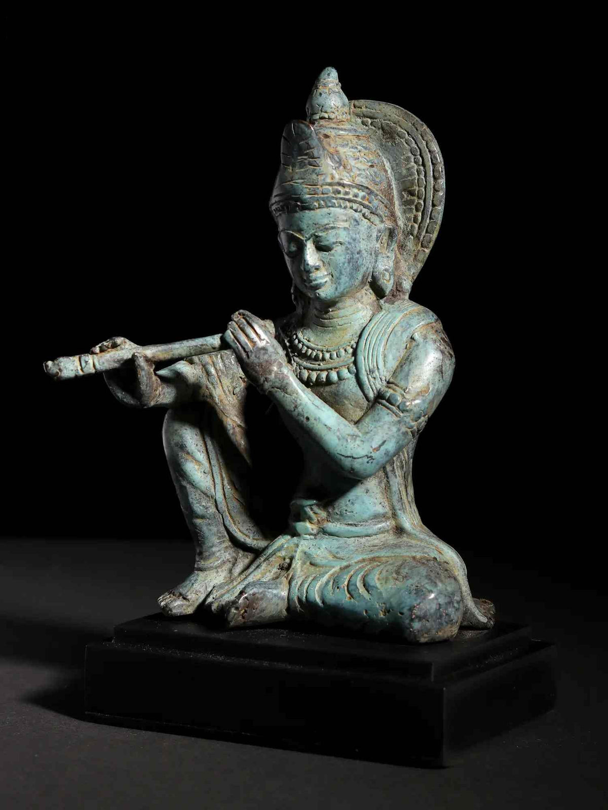 Seated brass Murli Manohar Krishna idol on dark wooden base, flute in hand