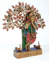 Brass Krishna statue playing flute beside decorated tree with leaf motifs, 16 in