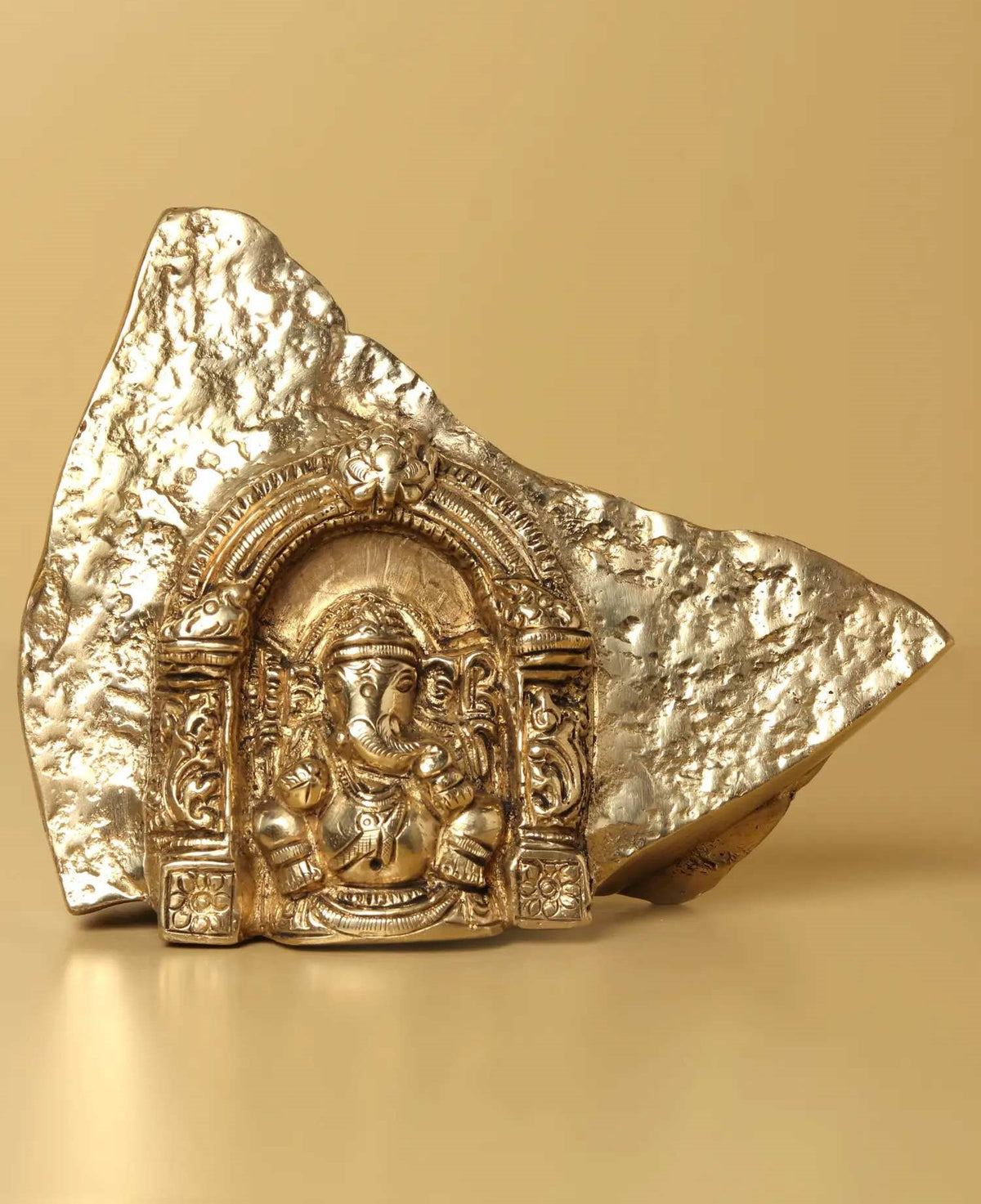 Natural brass Ganesha temple idol with carved head and arched halo, rock base
