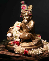 Seated brass Baby Krishna figurine on decorated base, hands near mouth