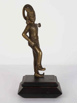 Brass Lord Krishna standing figure with one knee raised, on dark wooden pedestal