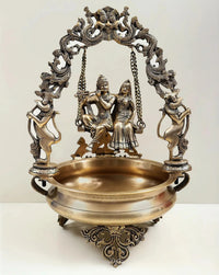 Brass urli with Radha Krishna on swing, ornate chain frame, 21-inch