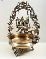 Brass urli centerpiece with Radha Krishna figurines on swing, detailed brass arch