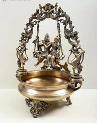 Brass urli centerpiece with Radha Krishna figurines on swing, detailed brass arch