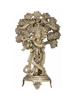 Brass Krishna statue playing flute under leafy tree, ornate detailing, on pedestal