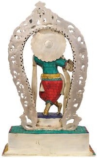 Rear view of brass Krishna statue with arched aureole and colorful outfit on base