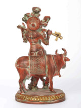 Lord Krishna on cow statue, circular headdress and drum details, red-gold brass