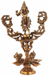 Brass devotional lamp with Lord Krishna figure, ornate swirl arms and multi-tier base