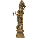 Brass Krishna figurine playing flute in profile, detailed armor and hanging ornaments.