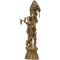 Brass Krishna figurine playing flute in profile, detailed armor and hanging ornaments.