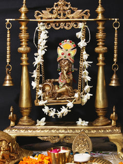 Handmade brass Krishna swing idol, seated figure with flower garland and beaded chains