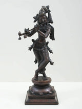 Brass-look standing Lord Krishna statue playing a flute, detailed headdress, on pedestal base