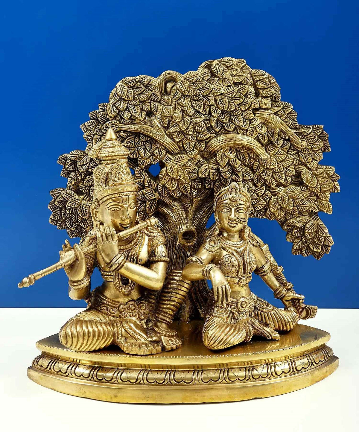 Brass Krishna and Radha flute statue, ornate tree canopy, kneeling pose on pedestal