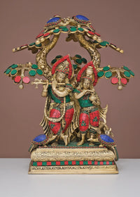 Brass Radha Krishna sculpture with jeweled tree, red and green accents on pedestal
