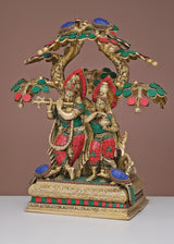 Brass Radha Krishna figurines beneath ornate tree canopy, painted red, green, blue details