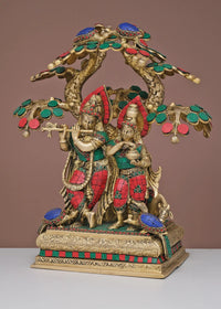 Brass Radha Krishna figurines beneath ornate tree canopy, painted red, green, blue details