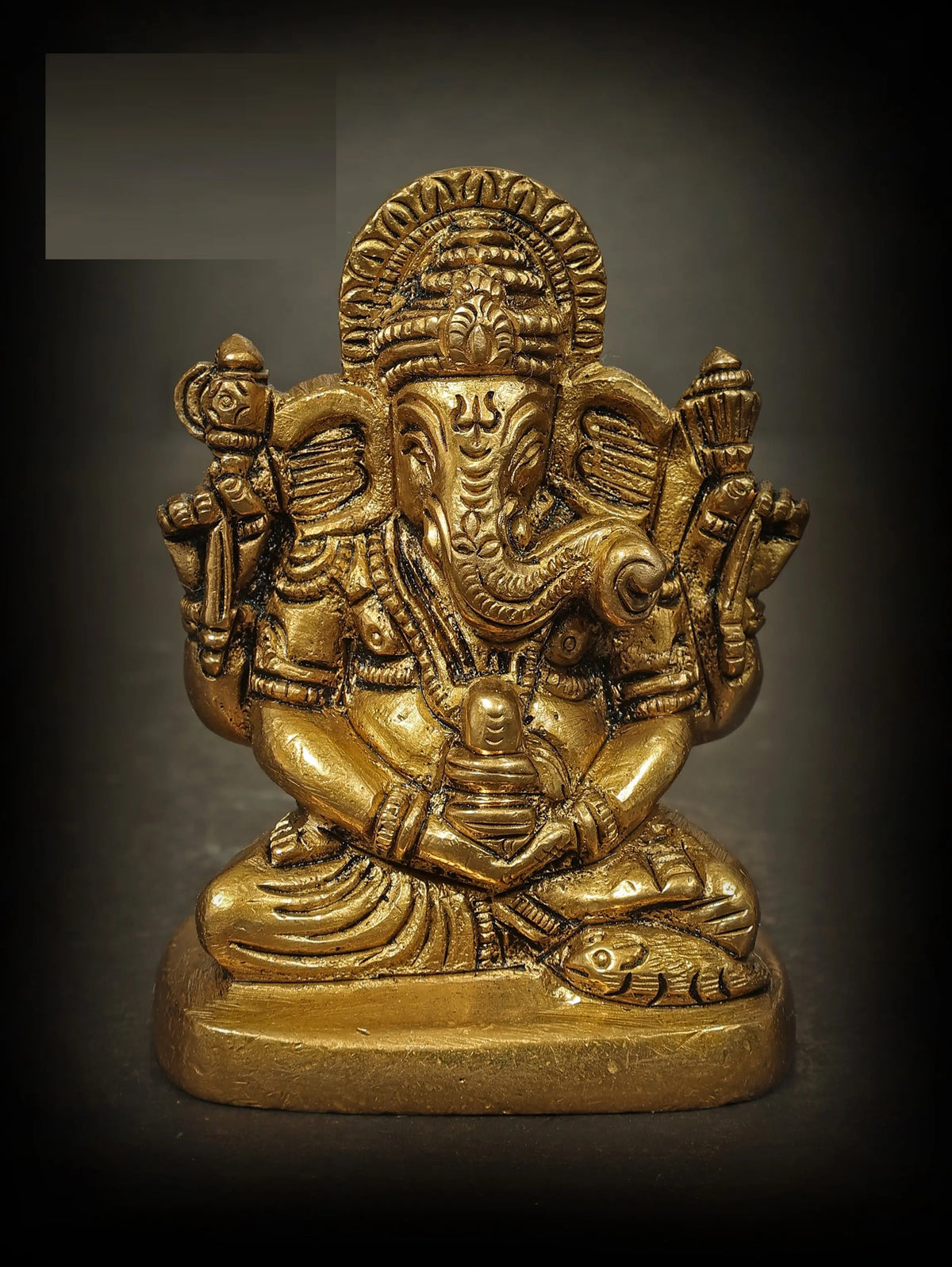 Small brass Ganesha sculpture, multi-armed, seated, holding a Shiva linga