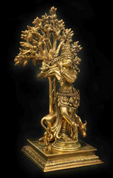 Brass Krishna statue in tribhanga pose holding flute, surrounded by detailed leaf tree