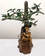 Brass Krishna playing flute figure beside twisting dark tree trunk and leaf canopy