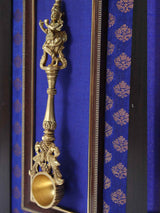 Close-up brass ritual spoon with Krishna figure and gold bowl in frame
