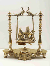 Brass peacock-perched swing statue of Radha and Krishna on ornate carved stand