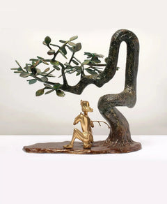 Standing brass Lord Krishna flute statue on base beneath arched leafy branches