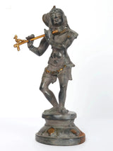 Lord Krishna statue in dark metal, playing a flute, standing on a pedestal