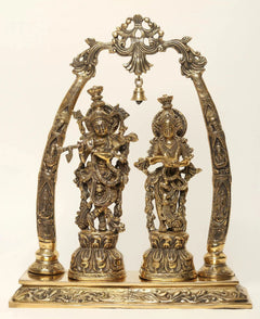 Brass Radha Krishna statue on tusk-style stand, ornate hanging bells and arch