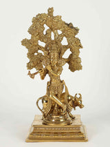 Lord Krishna brass statue under kalpavriksha, holding flute, with cow at base