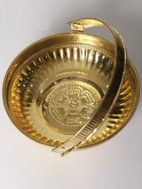 Brass pooja basket interior with Ganesha relief and ridged side pattern.