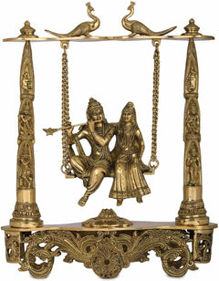Brass Radha Krishna statue on peacock swing, ornate posts and hanging chains