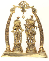 Brass Radha Krishna statue with carved arched frame and two figurines, bell hanging