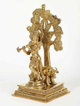 Brass Krishna figure beside kalpavriksha tree with carved foliage and cow
