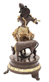 Rear view of brass Venugopala idol on dark brown circular base, gold ornamentation