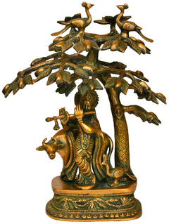 Brass Krishna playing flute statue under mango tree, decorative leaves and base