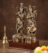 Brass Radha Krishna statue on elephant-shaped pedestal bases, ornate finish on wooden platform