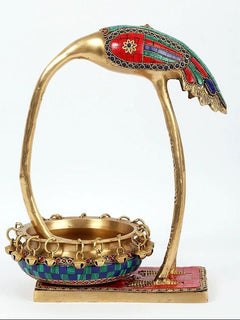 Side view of brass leaning flamingo urli with jeweled mosaic patch and chain bowl