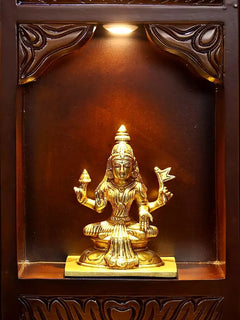 Gold-toned deity idol with raised arms on base inside a brass niche