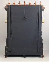 Back of brass mandir with dark panel, hanging cords, and four corner feet