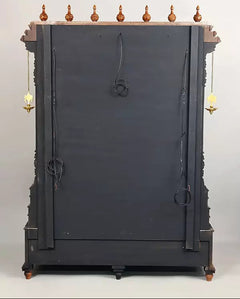 Back of brass mandir with dark panel, hanging cords, and four corner feet