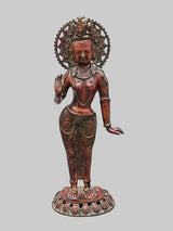Standing Tara brass idol with ornate halo, seated smile, raised right hand