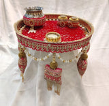 Red embellished steel pooja thali with golden rim, small containers and beaded tassels